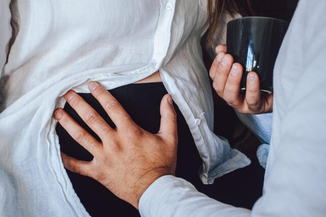 Pregnant Maghrebi woman in contemporary setting, holding baby while surrounded by traditional decor and modern appliances.