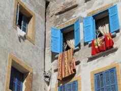 Exploring the ‘St Tropez of North Africa’: Essaouira, Morocco – A Budget Travel Guide woman walking on essaouira beach, moroccan architecture in the background